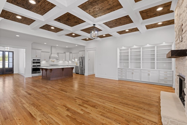 unfurnished living room with baseboards, a notable chandelier, light wood-type flooring, a fireplace, and beam ceiling