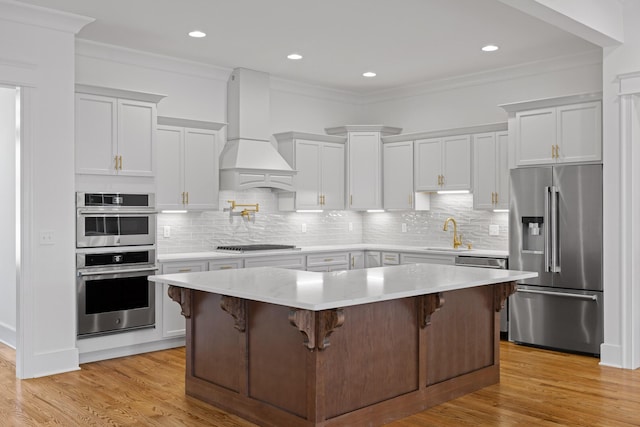 kitchen with light wood finished floors, appliances with stainless steel finishes, custom exhaust hood, light countertops, and a sink