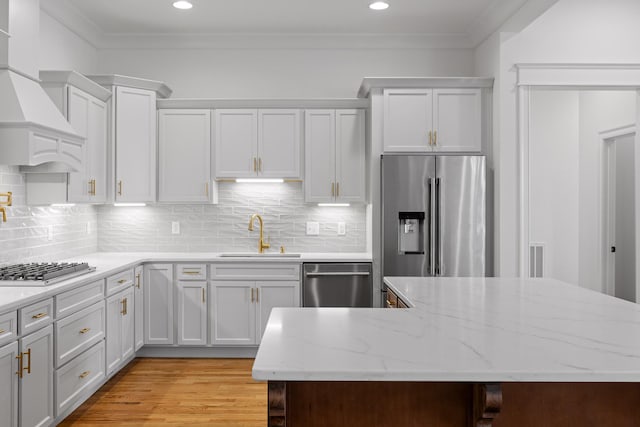 kitchen with stainless steel appliances, backsplash, light wood-style floors, ornamental molding, and a sink