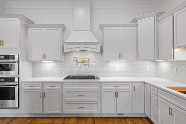 kitchen with stainless steel double oven, gas stovetop, white cabinetry, and custom range hood