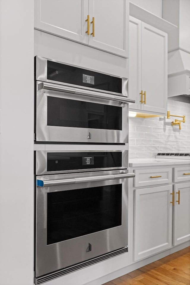 kitchen featuring double oven, light countertops, light wood finished floors, cooktop, and tasteful backsplash