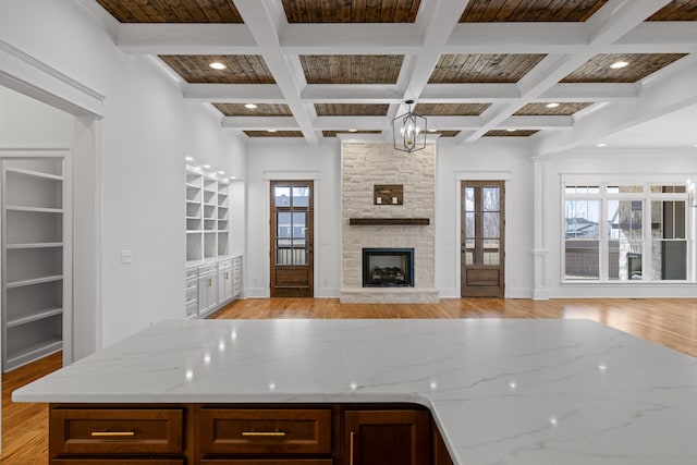 kitchen featuring beam ceiling, open floor plan, light wood finished floors, and light stone countertops