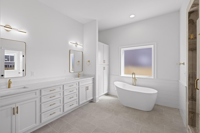 full bathroom featuring a sink, tile walls, a freestanding bath, and double vanity