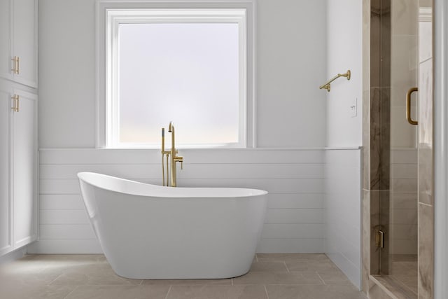 full bath featuring a wainscoted wall, tile walls, a soaking tub, a stall shower, and tile patterned floors