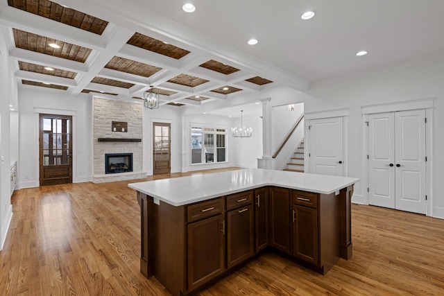 kitchen featuring light wood finished floors, a fireplace, a chandelier, and beamed ceiling