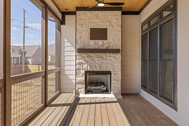 unfurnished sunroom featuring an outdoor stone fireplace, wood ceiling, and a ceiling fan