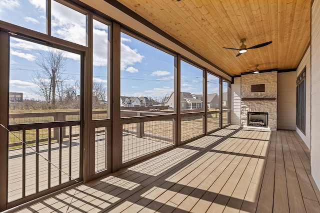 unfurnished sunroom with ceiling fan, a stone fireplace, and wood ceiling