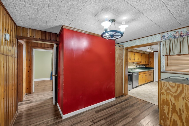 kitchen featuring wood walls, a sink, wood finished floors, stainless steel dishwasher, and an inviting chandelier