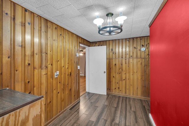 corridor featuring a notable chandelier, wood walls, baseboards, and wood finished floors