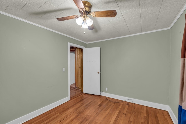 spare room featuring ornamental molding, wood finished floors, a ceiling fan, and baseboards