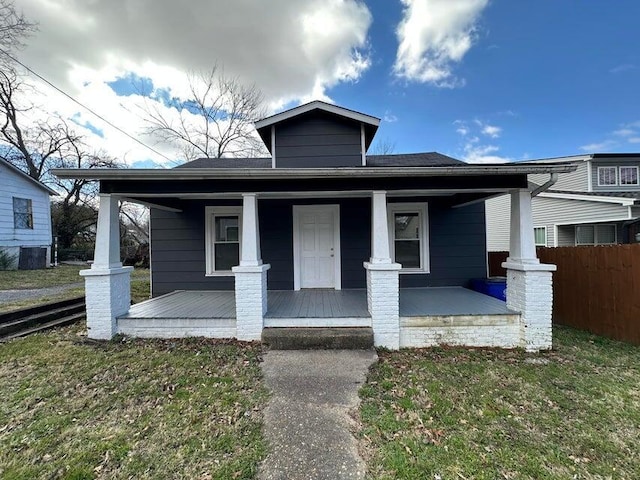 bungalow with covered porch, fence, and a front lawn