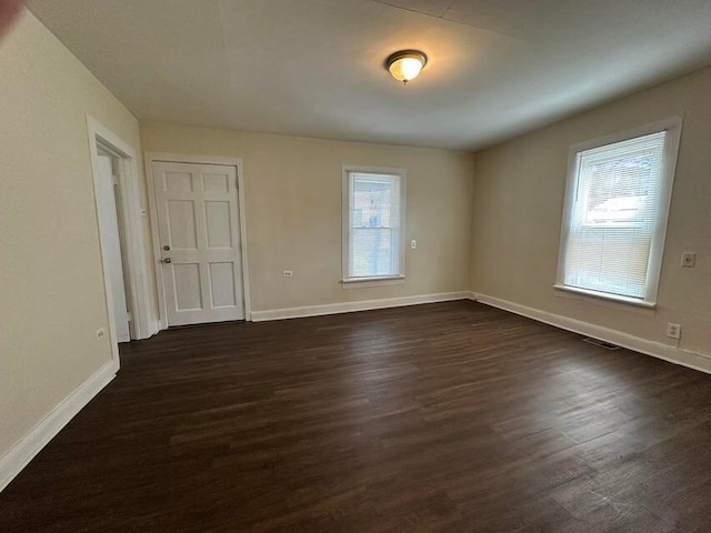 spare room with dark wood-style floors, visible vents, and baseboards