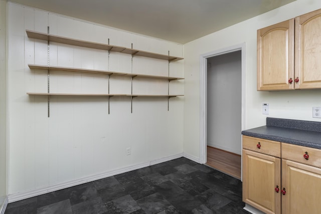 interior space featuring light brown cabinetry, stone finish floor, open shelves, dark countertops, and baseboards