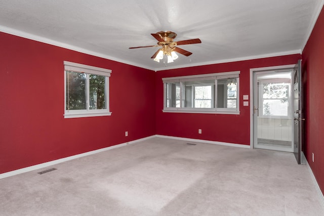 carpeted empty room featuring visible vents, baseboards, a ceiling fan, and crown molding