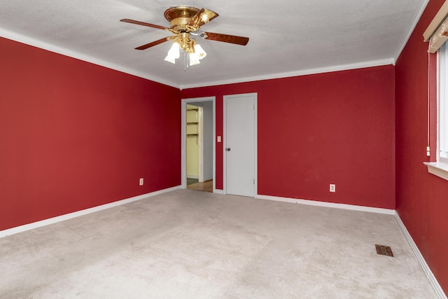 carpeted spare room with baseboards, visible vents, ceiling fan, ornamental molding, and a textured ceiling