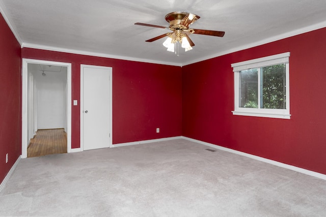 empty room with visible vents, a ceiling fan, carpet floors, crown molding, and baseboards