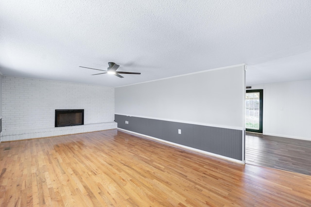 unfurnished living room featuring baseboards, a fireplace, wood finished floors, a textured ceiling, and a ceiling fan