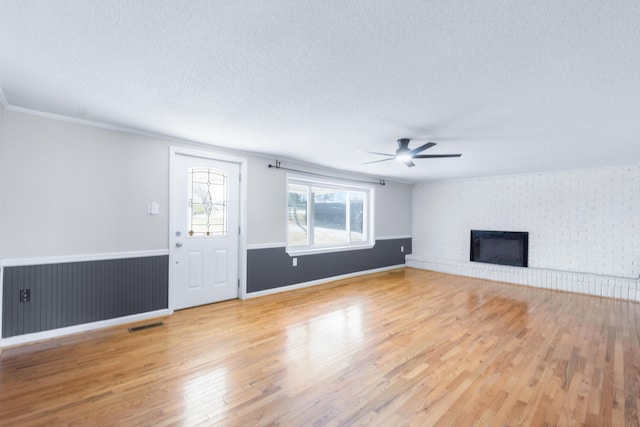 unfurnished living room featuring wood finished floors, a fireplace, ceiling fan, ornamental molding, and a textured ceiling