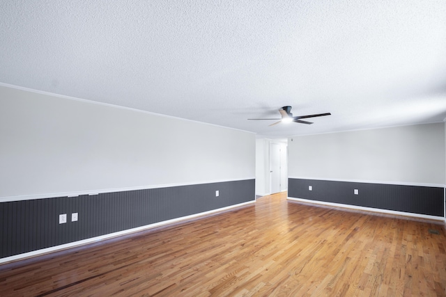 spare room featuring wainscoting, a textured ceiling, a ceiling fan, and wood finished floors