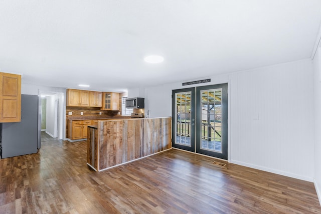 kitchen featuring glass insert cabinets, dark wood finished floors, french doors, a peninsula, and stainless steel appliances