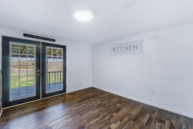 empty room with a textured ceiling, dark wood finished floors, french doors, crown molding, and baseboards