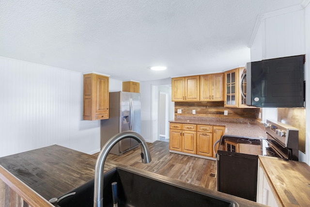 kitchen with a sink, a textured ceiling, wood finished floors, appliances with stainless steel finishes, and glass insert cabinets