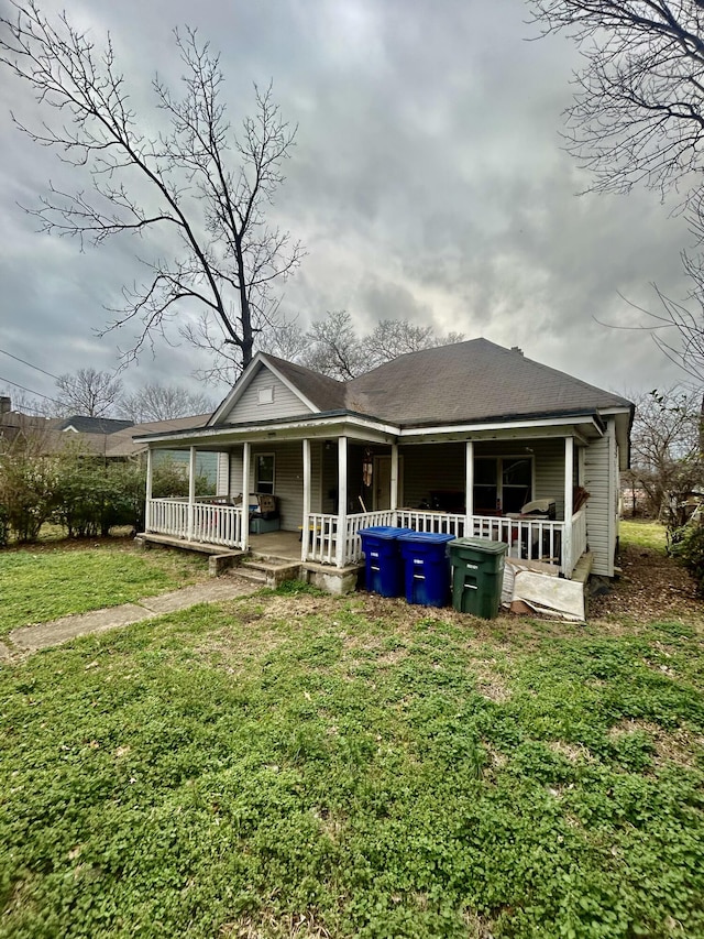 rear view of property with a shingled roof, covered porch, and a lawn