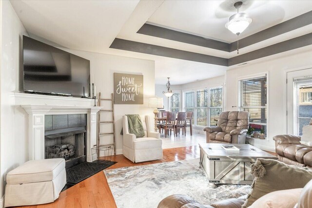 living room featuring a tray ceiling, ceiling fan, a tiled fireplace, and wood finished floors