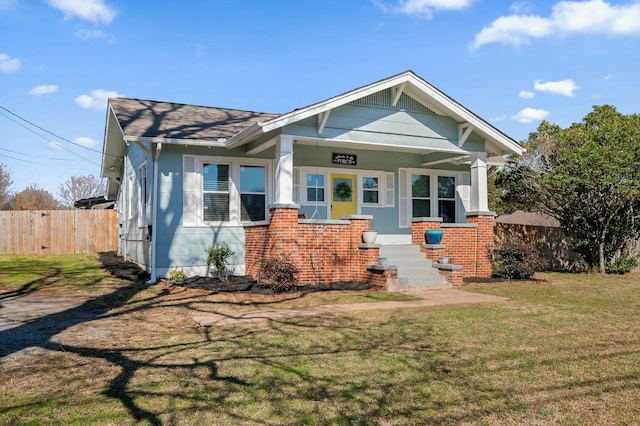 view of front of home with brick siding, covered porch, a front lawn, and fence