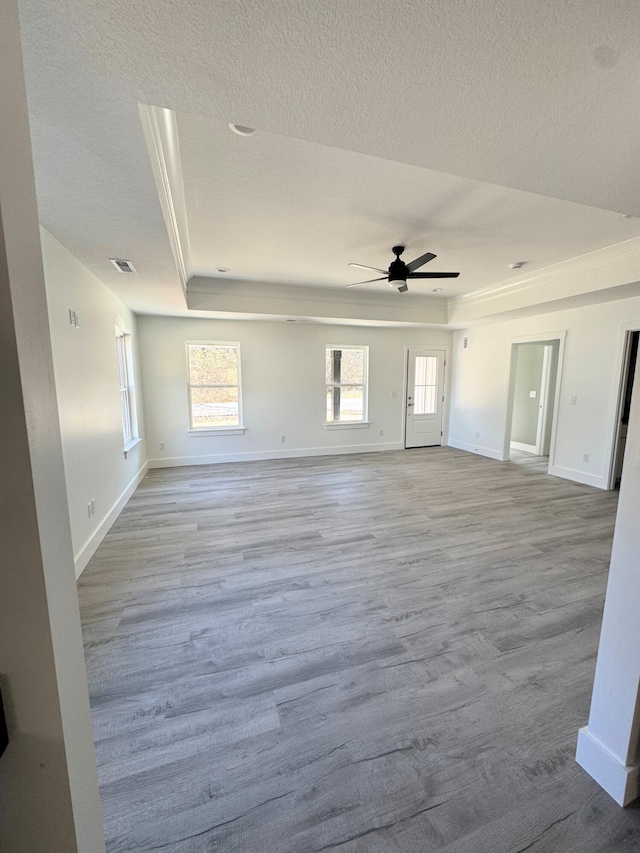 unfurnished living room featuring baseboards, visible vents, a ceiling fan, a raised ceiling, and wood finished floors