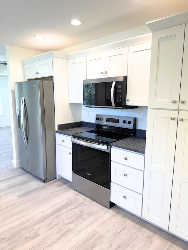 kitchen featuring appliances with stainless steel finishes, dark countertops, white cabinetry, and light wood-style floors