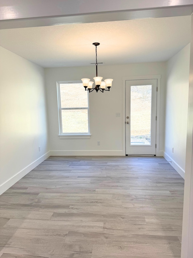 unfurnished dining area with baseboards, light wood finished floors, and an inviting chandelier