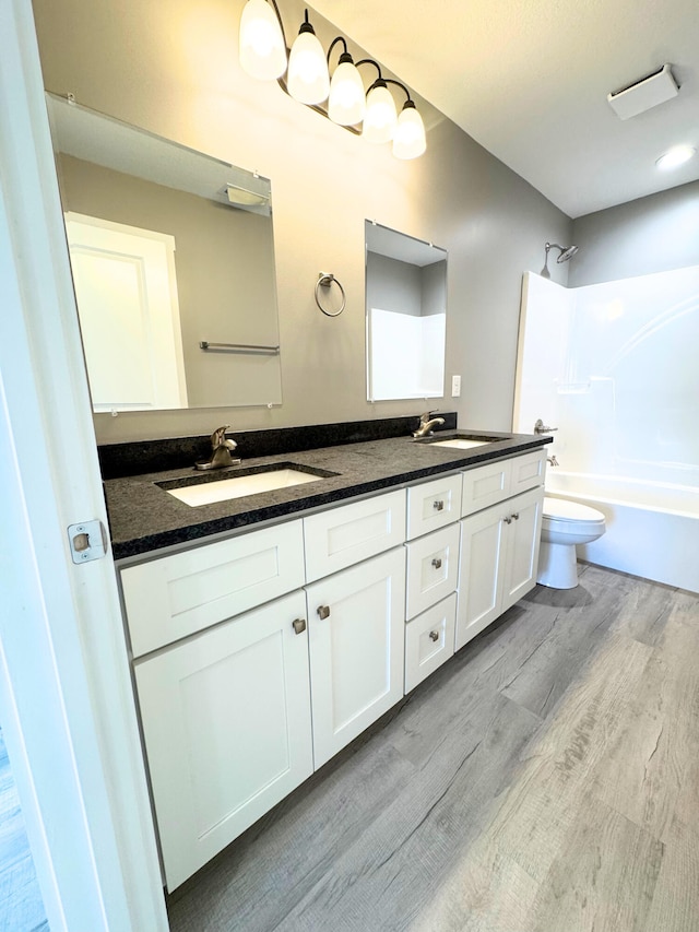 bathroom featuring double vanity, toilet, a sink, and wood finished floors