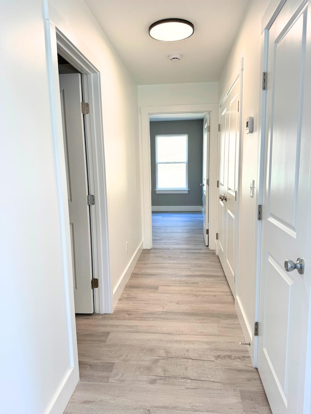 corridor featuring light wood-style flooring and baseboards