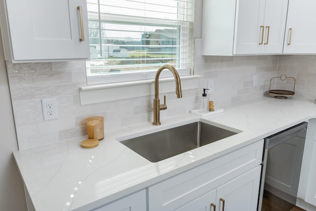 kitchen featuring light stone counters, decorative backsplash, white cabinets, a sink, and dishwasher