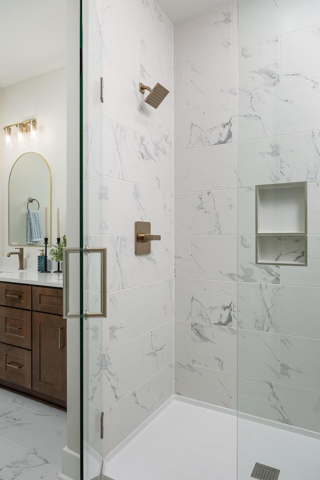 bathroom featuring marble finish floor, tiled shower, and vanity