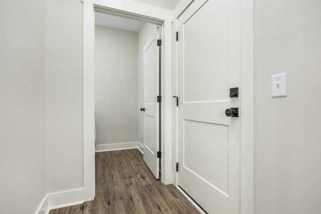 corridor featuring dark wood-type flooring and baseboards