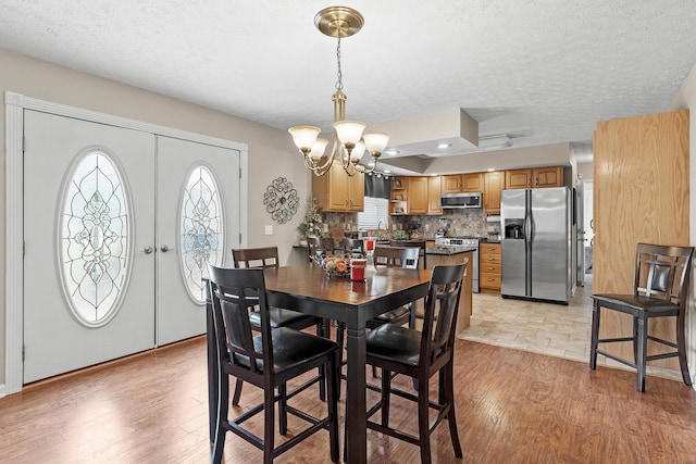 dining space with a textured ceiling, french doors, an inviting chandelier, and light wood-style floors