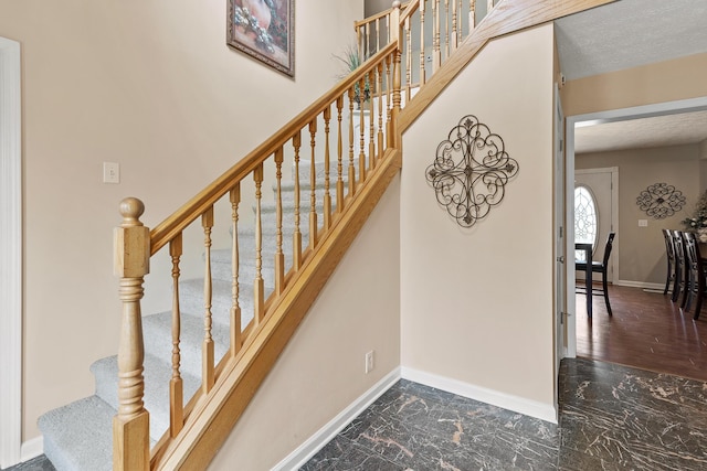 staircase featuring marble finish floor, a textured ceiling, and baseboards