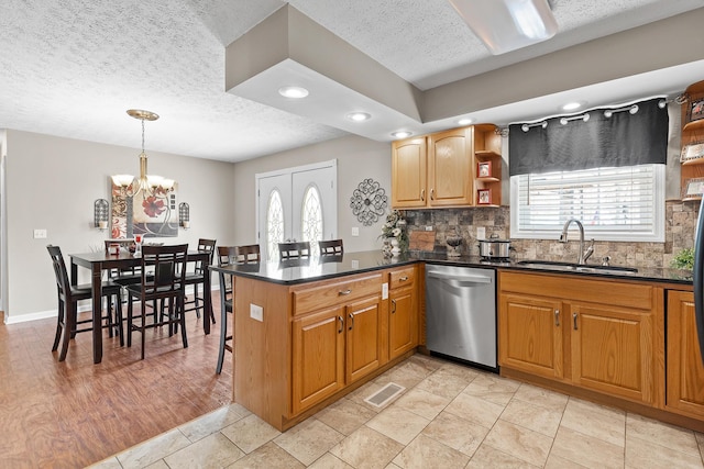 kitchen featuring tasteful backsplash, visible vents, stainless steel dishwasher, a sink, and a peninsula