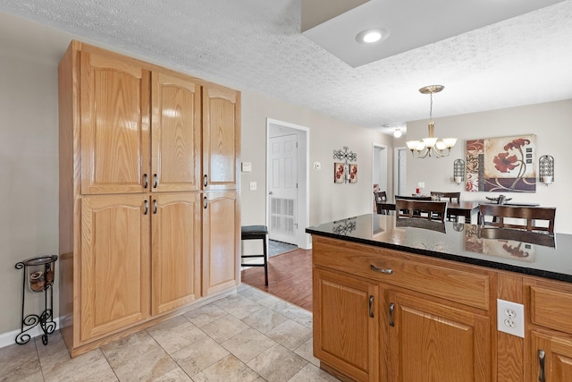 kitchen featuring hanging light fixtures, dark stone countertops, a chandelier, and a textured ceiling