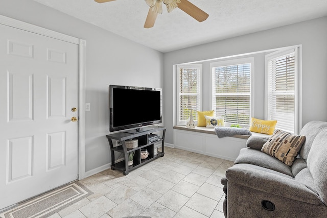 living area with a textured ceiling, a ceiling fan, and baseboards