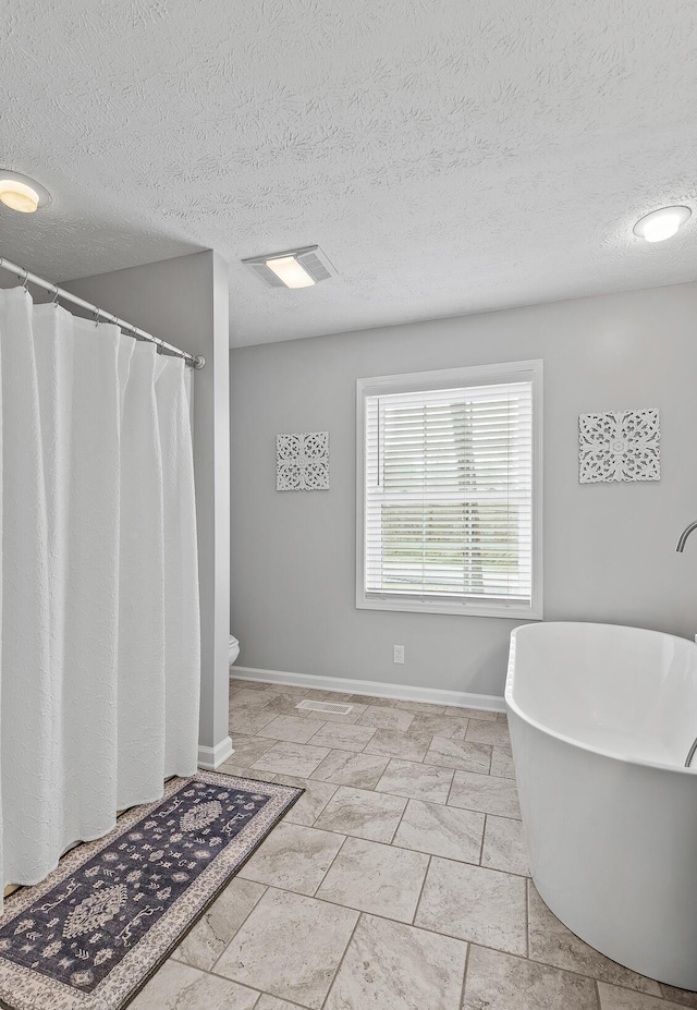 full bath featuring a textured ceiling, toilet, a shower with shower curtain, baseboards, and a soaking tub