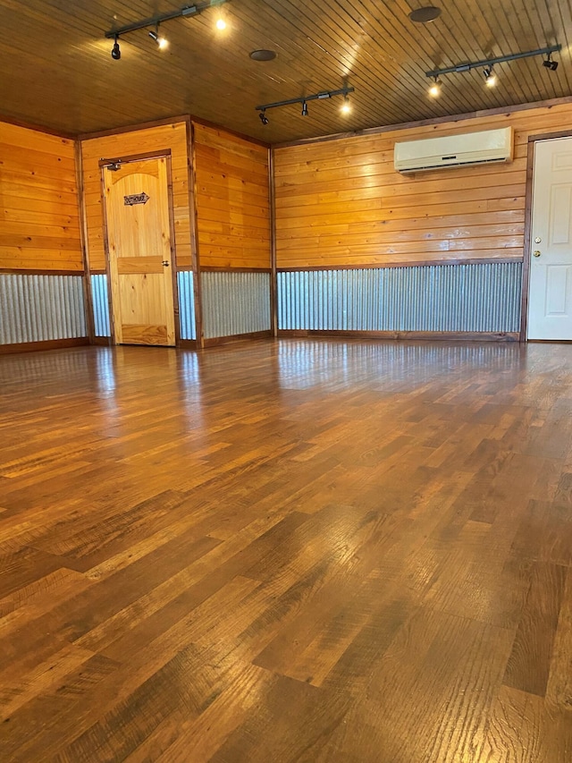 unfurnished room featuring track lighting, a wall mounted air conditioner, wood finished floors, and wooden walls