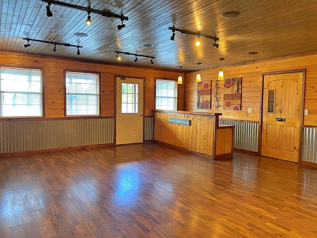 unfurnished living room featuring dark wood-style floors, wood walls, and rail lighting