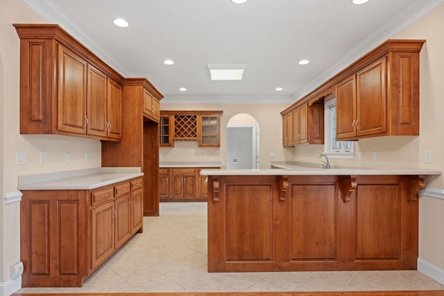 kitchen with arched walkways, brown cabinets, crown molding, and a peninsula