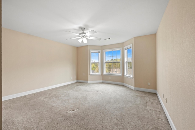 carpeted spare room with visible vents, baseboards, and a ceiling fan