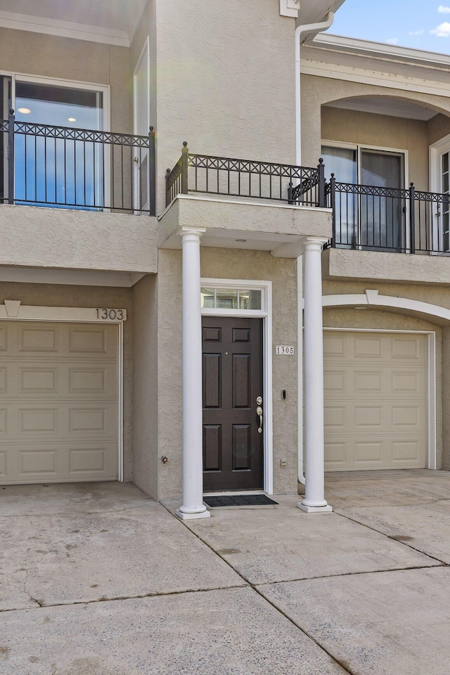 property entrance with a garage, a balcony, driveway, and stucco siding