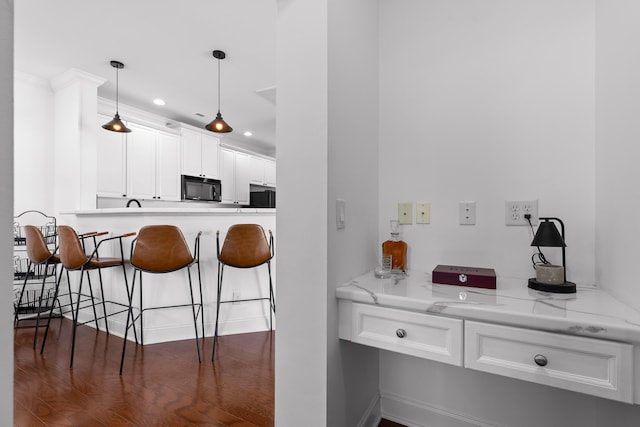 kitchen with dark wood finished floors, hanging light fixtures, black microwave, white cabinetry, and a kitchen breakfast bar