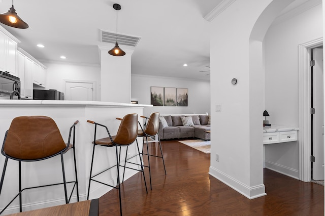 kitchen featuring visible vents, a kitchen bar, arched walkways, white cabinets, and dark wood-style flooring